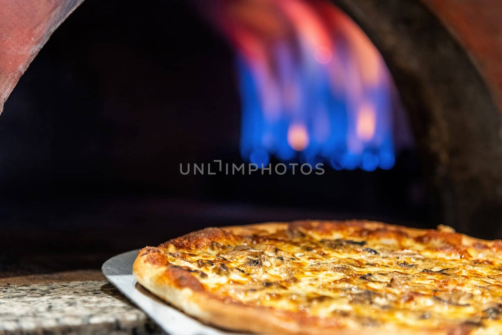 Mixed pizza fresh from the pizza oven with flames visible in the background