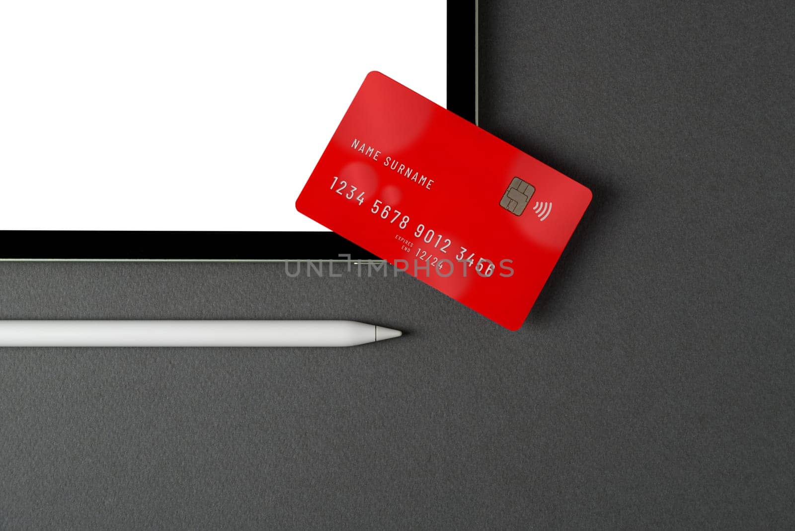 Credit card lying on tablet with blank screen on dark gray table