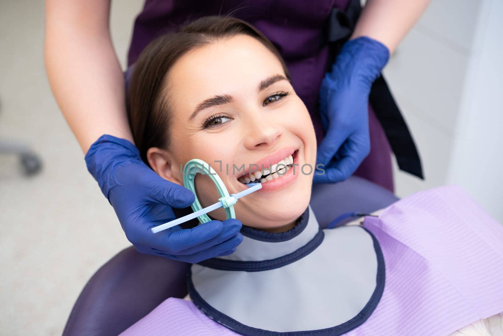 Dental assistant prepares patient for X-ray using specialized tools in clinic. Woman asks female patient to smile for better view of mouth