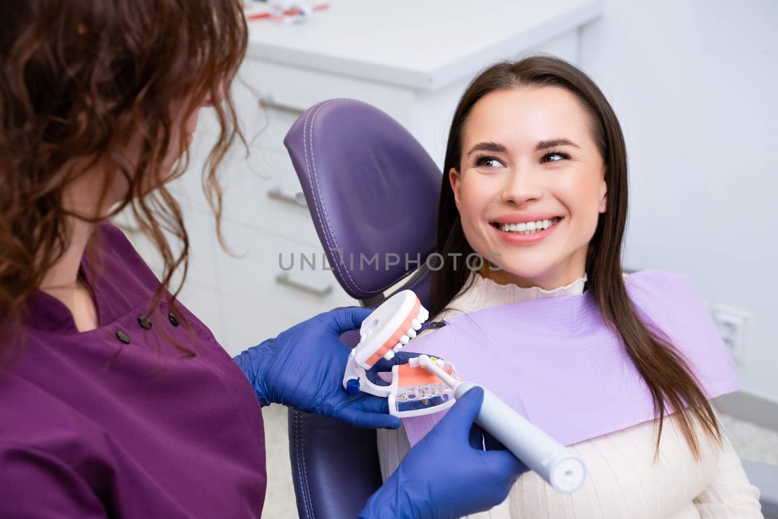 Dental professional explains to female patient how to brush teeth correctly in clinic. Dentists uses human jaw dental model for clarity