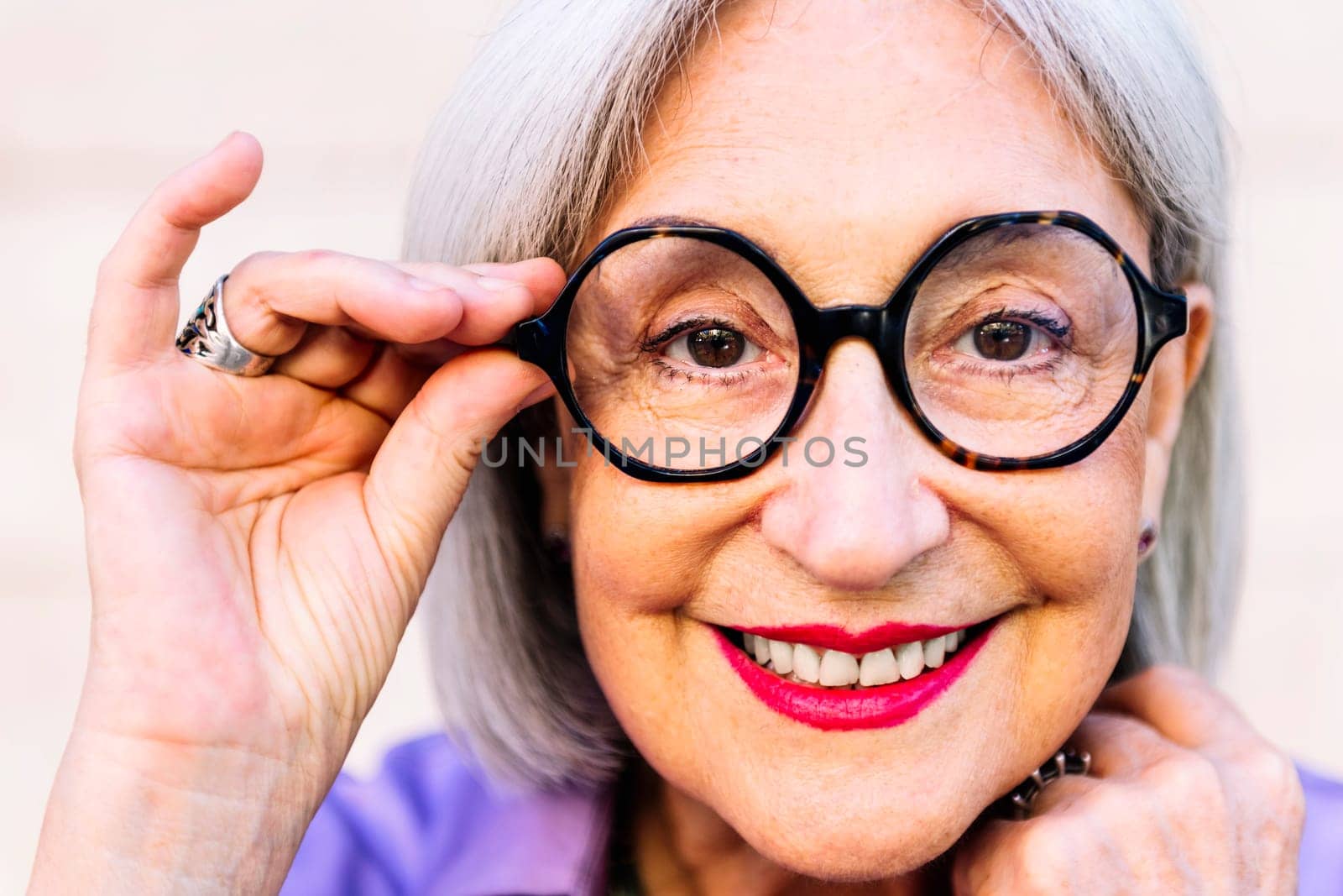 close-up portrait of a beautiful smiling senior woman putting on glasses, concept of happiness of elderly people and active lifestyle