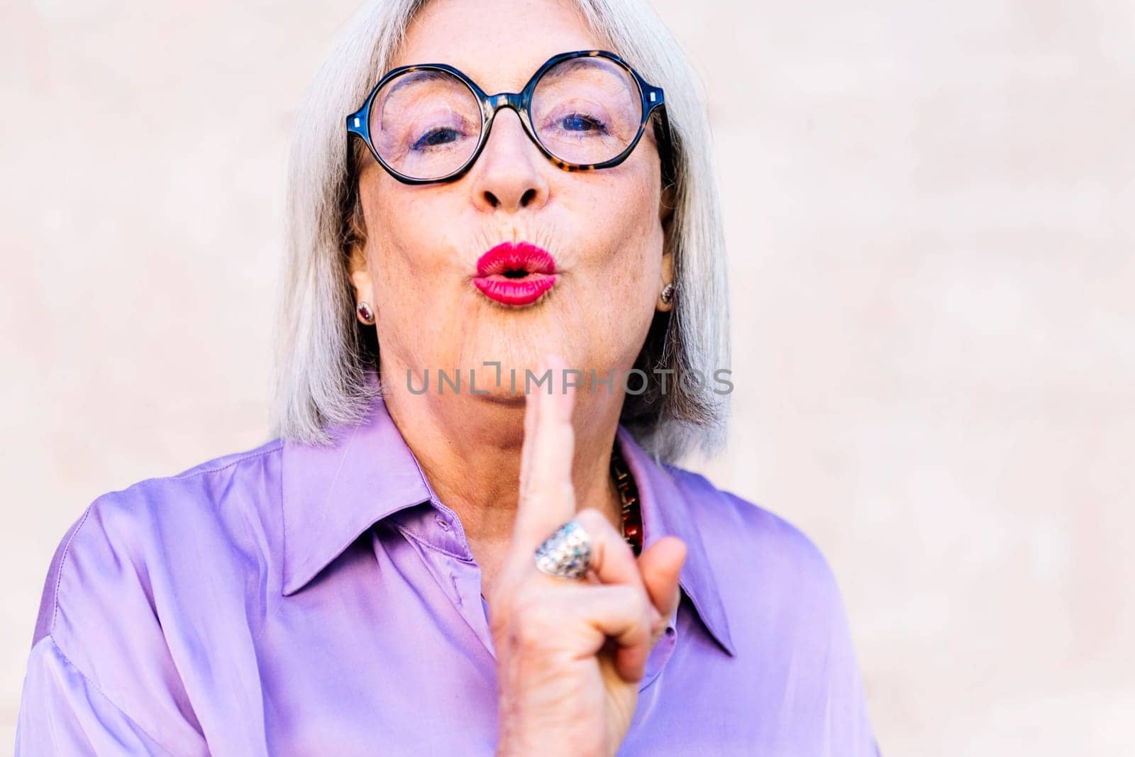 portrait of a nice senior woman blowing on her fingers like a gun after shooting, concept of happiness of elderly people and active lifestyle