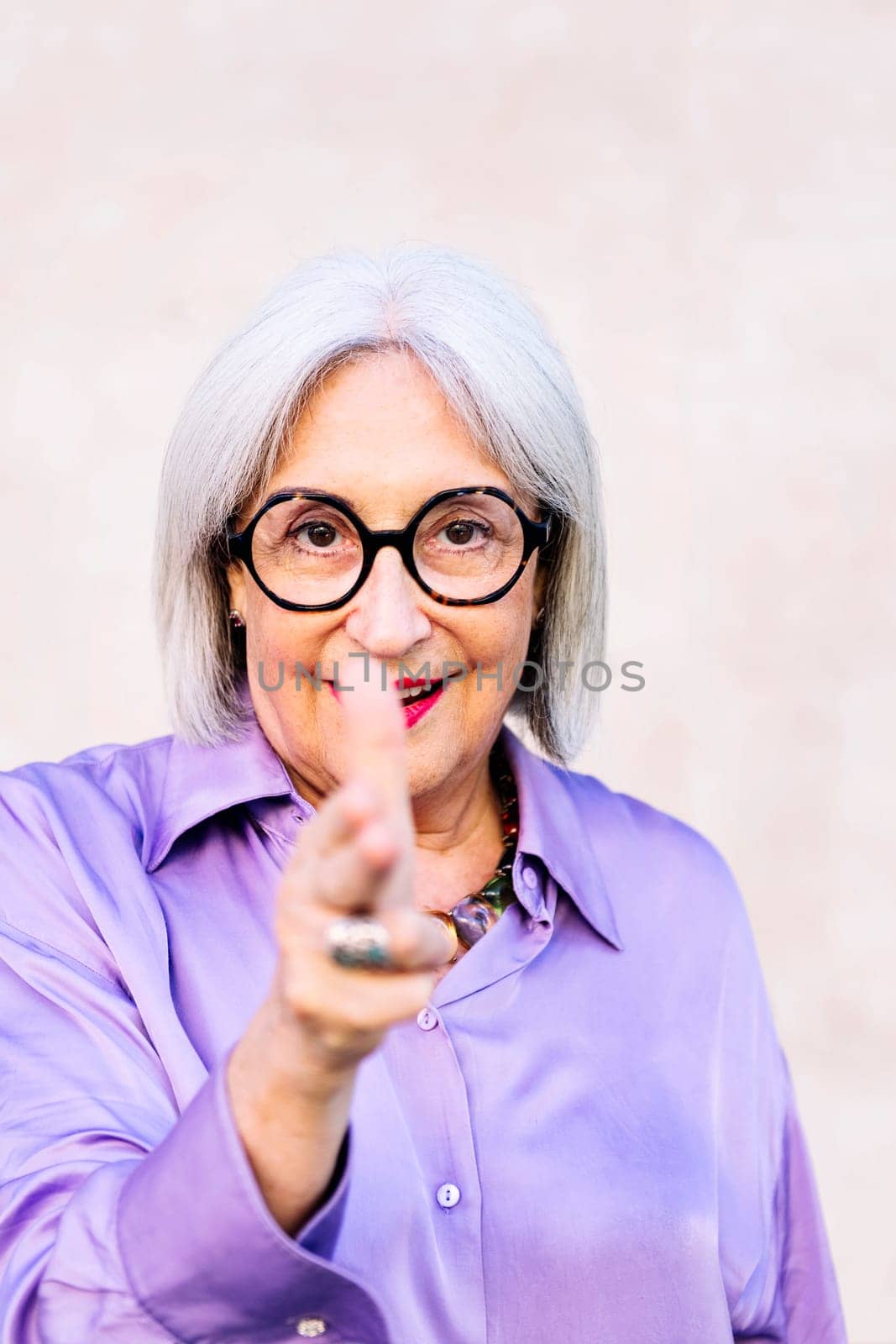 friendly senior woman looking at camera pointing with fingers like a gun, concept of happiness of elderly people and active lifestyle