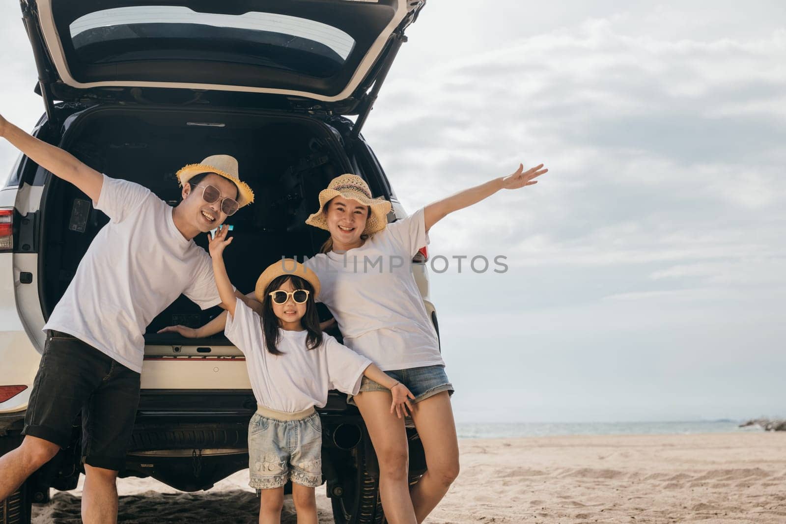 Happy Family Day. People enjoying road trip standing on back their car raise arms and hand up, Father, Mother and daughter traveling at sea beach, small family having fun in summer vacation on beach