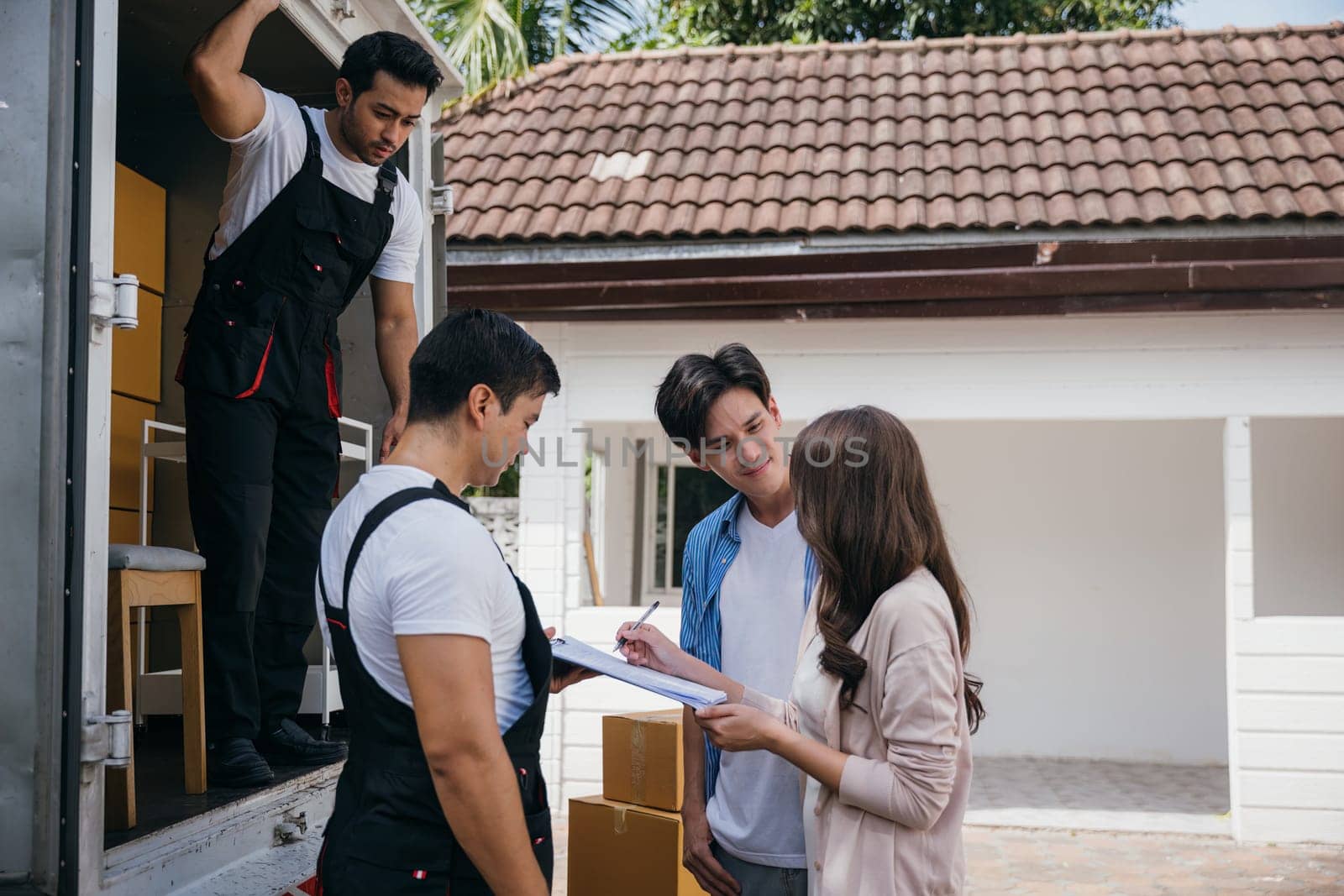 Newlyweds satisfied sign the delivery checklist with the professional moving team after furniture handling. Employees' teamwork assures customer happiness. Moving Day Concept by Sorapop