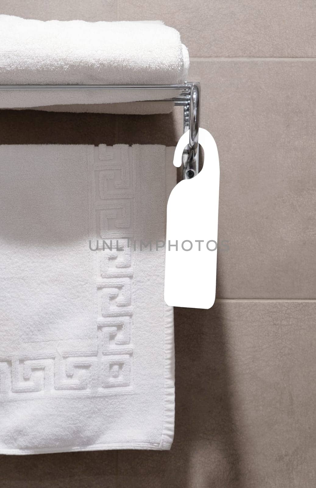 Set of white towels in the bathroom of a hotel room hung on a hanger with blank tag for mockup