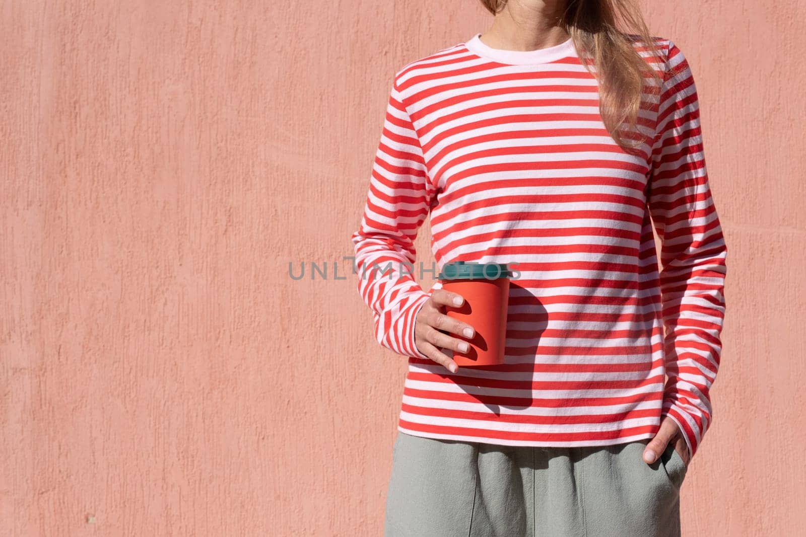 Woman in striped shirt holding red cup and drinking coffee. Close up hand with paper cup.