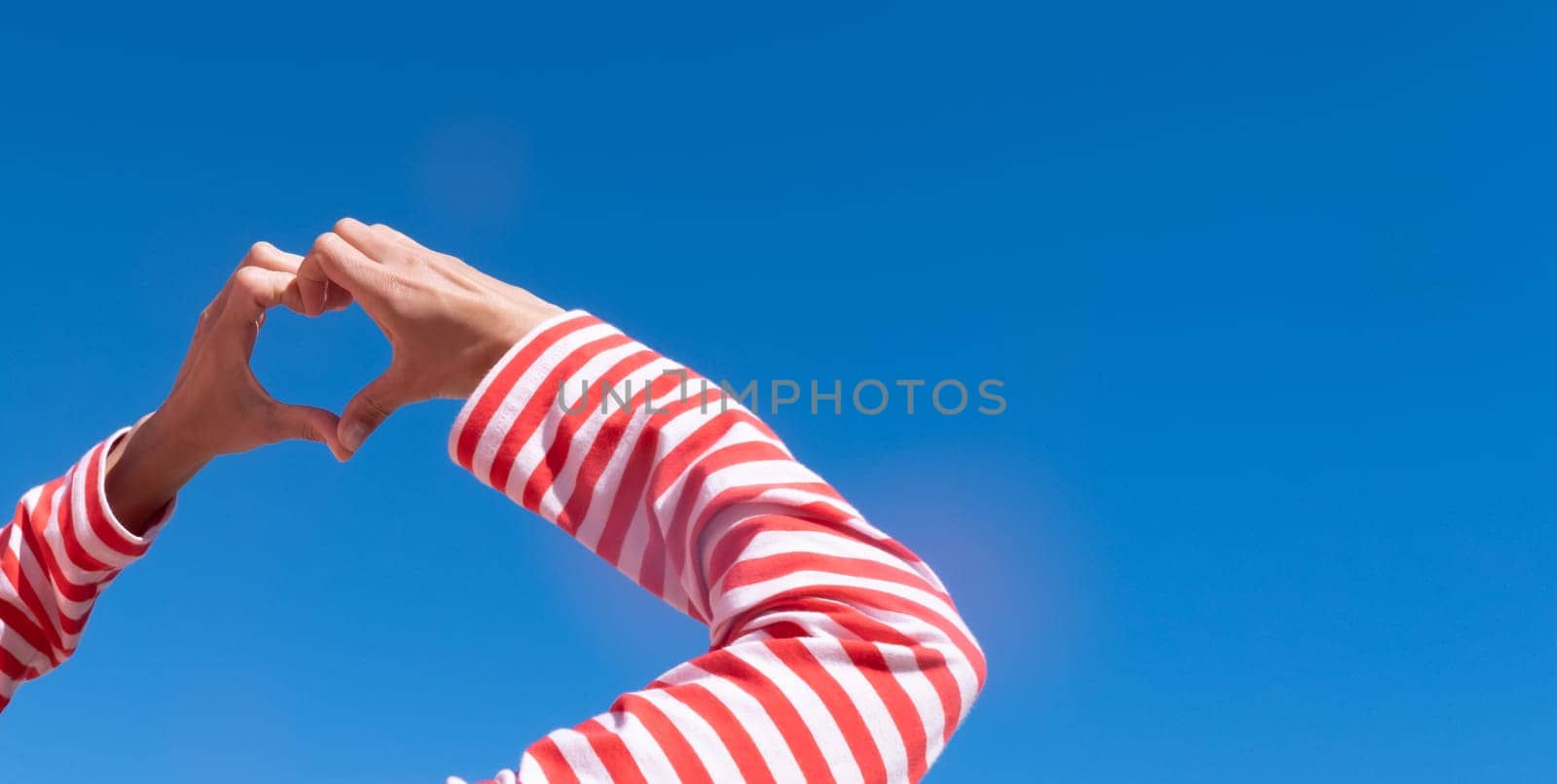 Female hands making sign Heart by fingers on sky background. Beautiful hands of woman with copy space. Love concept on Valentine day.