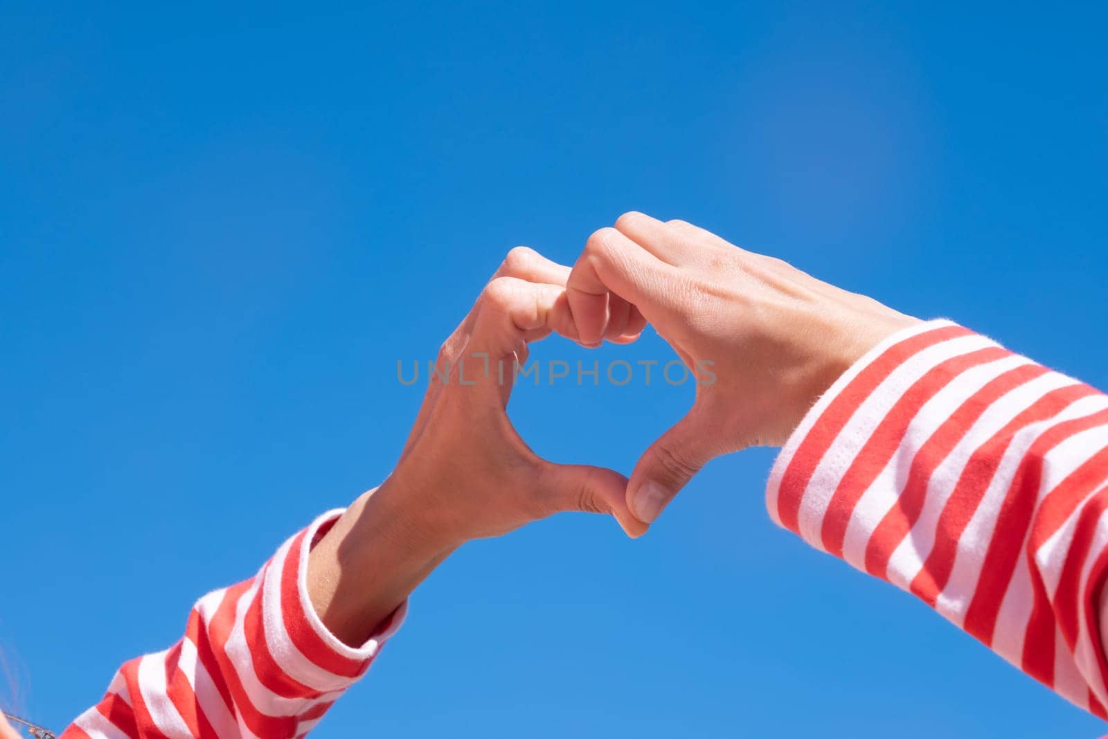 Female hands making sign Heart by fingers on sky background. Beautiful hands of woman with copy space. Love concept on Valentine day.