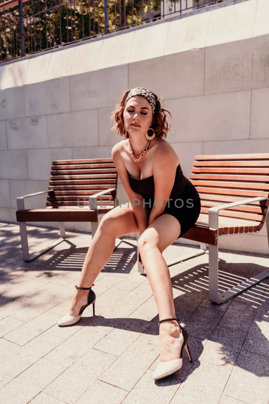 Portrait of a woman on the street. An attractive woman in a black dress is sitting on a bench outside