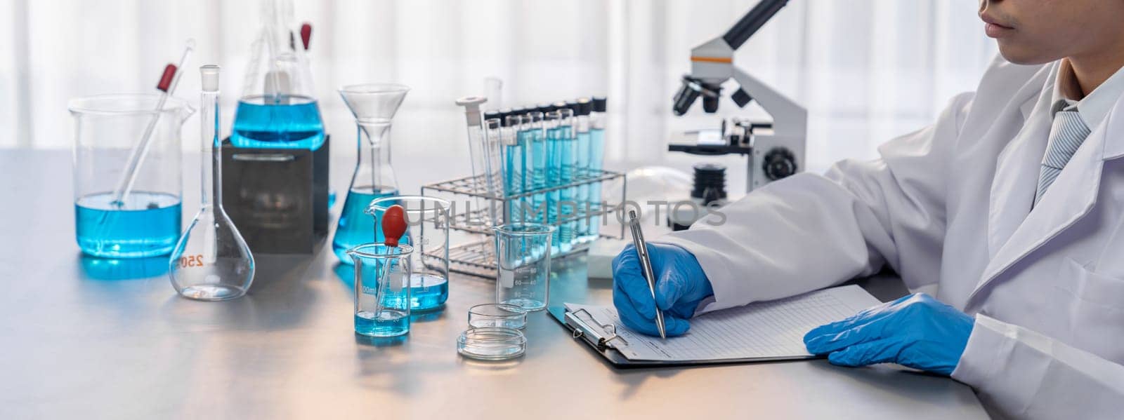 Closeup hand recording clinical data result after conducting chemical experiment in medical laboratory for vaccine drug or antibiotic. Scientific chemistry lab and medicine research concept. Neoteric