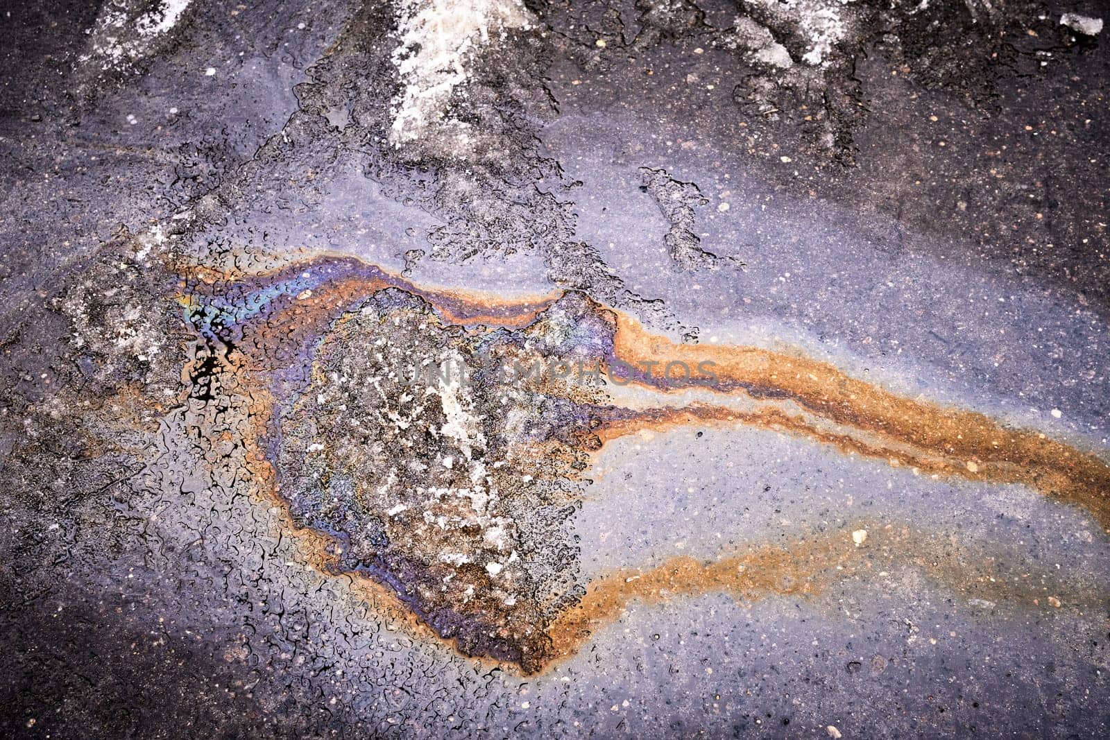 A bright spot of oil or gasoline splash on the asphalt after the snow melts.
