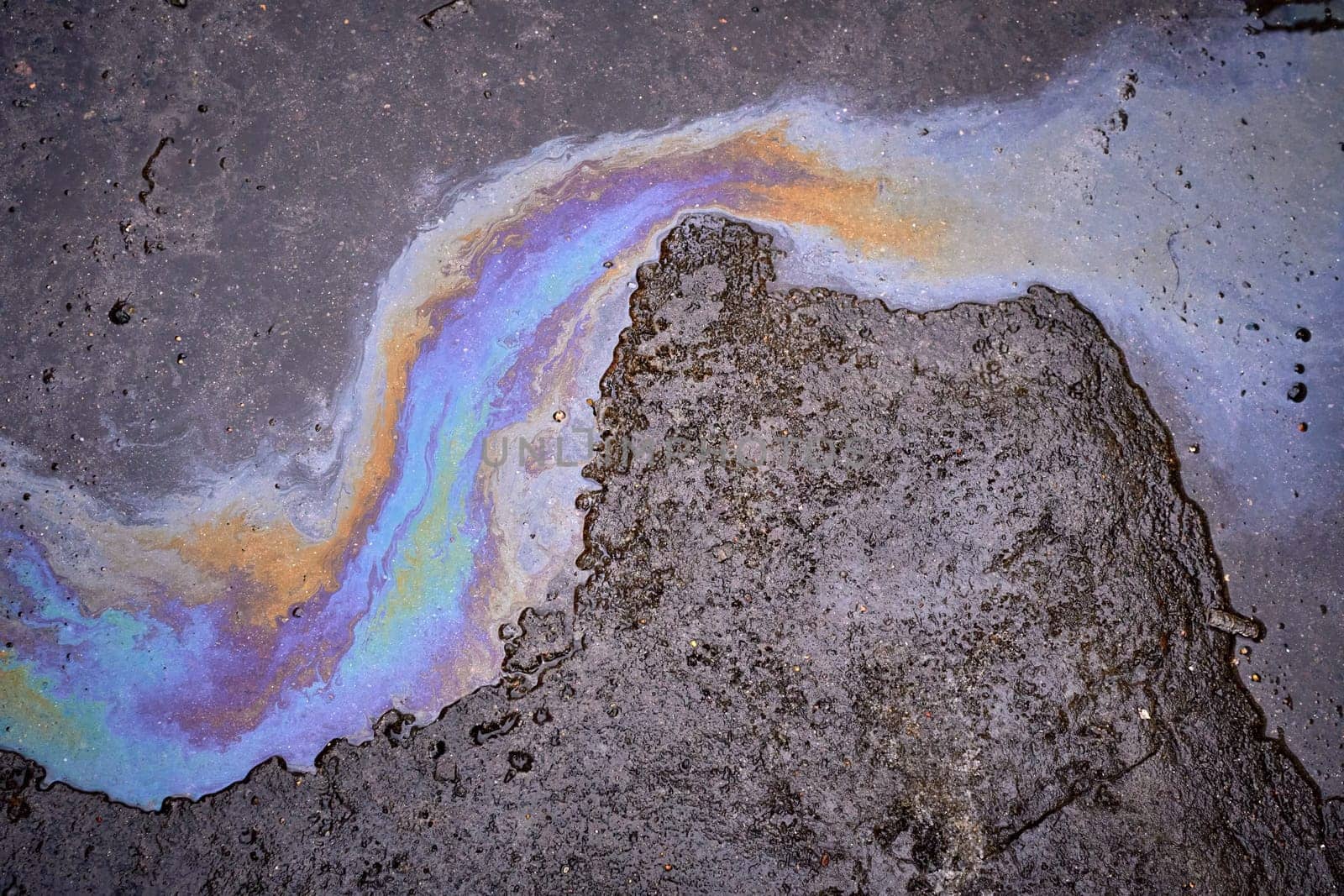 Leakage of oil or gasoline from under the car on the asphalt in the parking lot.