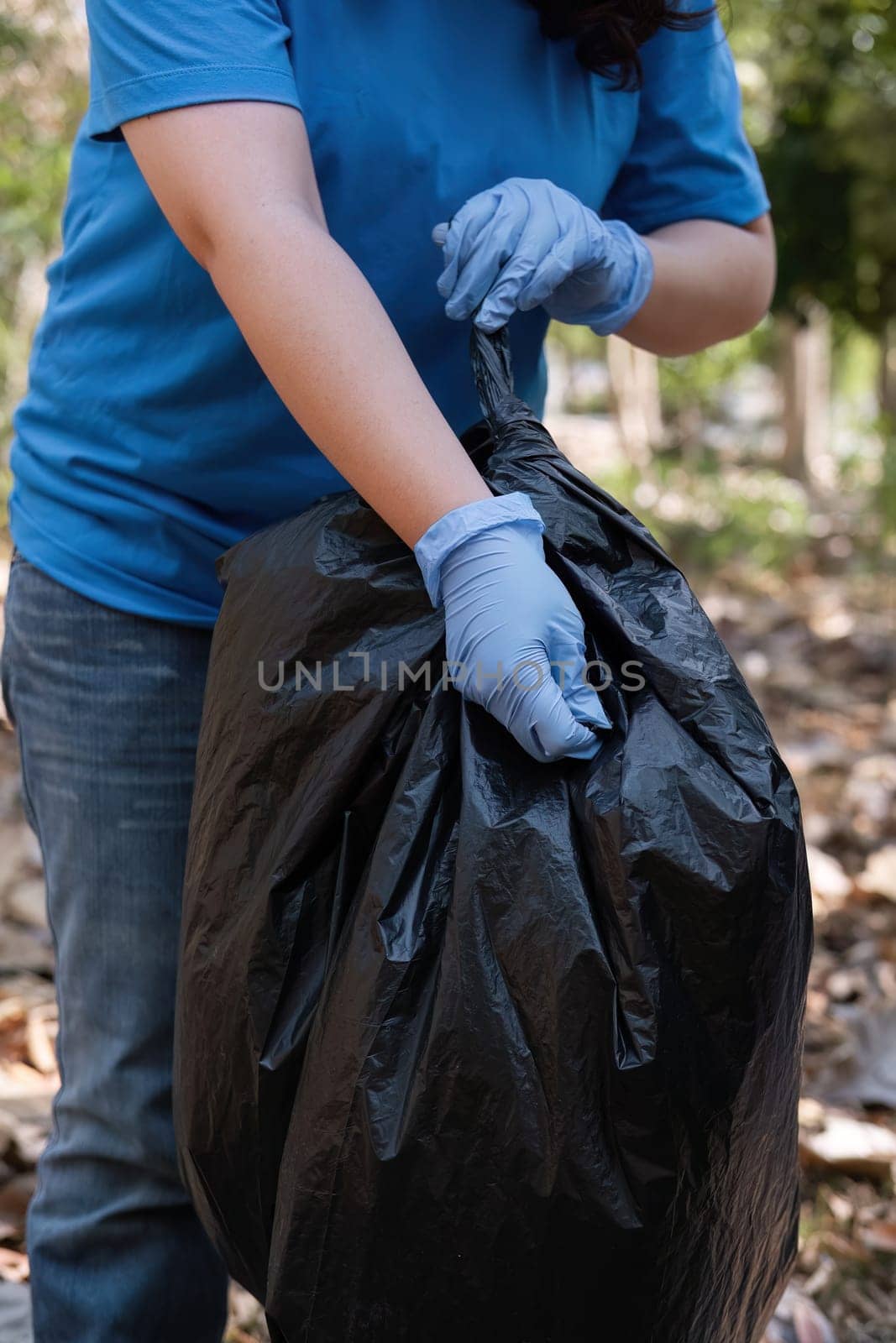 Up close, a group of Asian volunteers collects trash in plastic bags and cleans areas in the forest to preserve the natural ecosystem. by wichayada