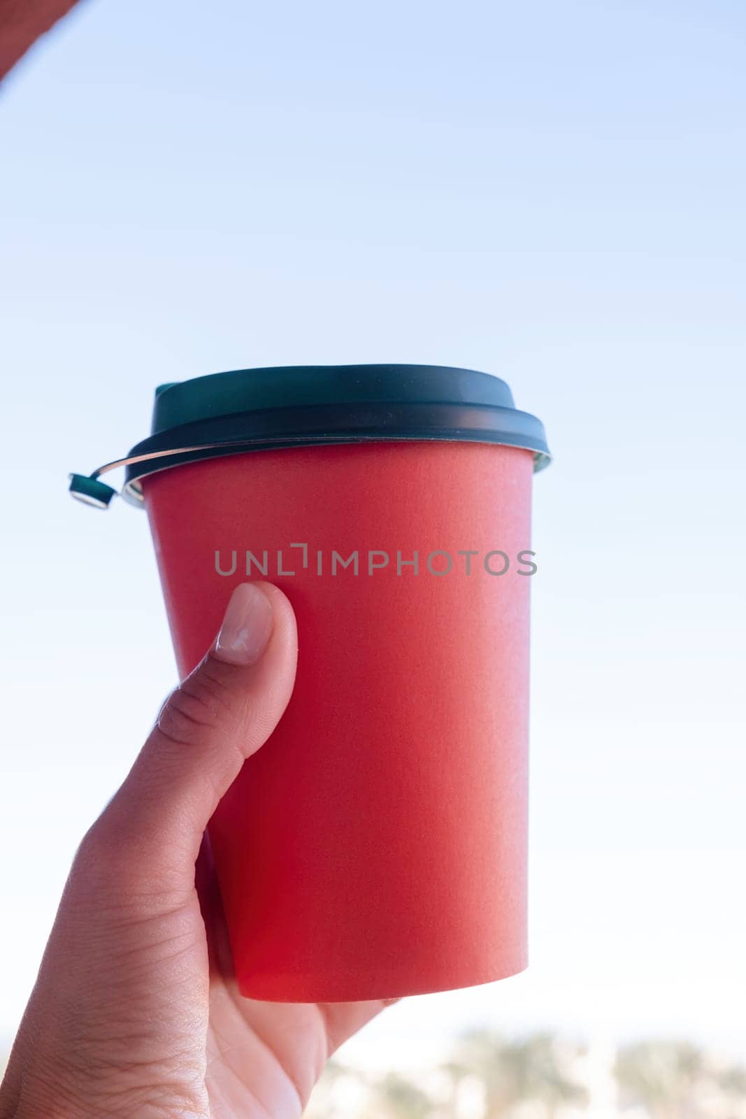 hand holding red paper coffee cup on sky background by Desperada