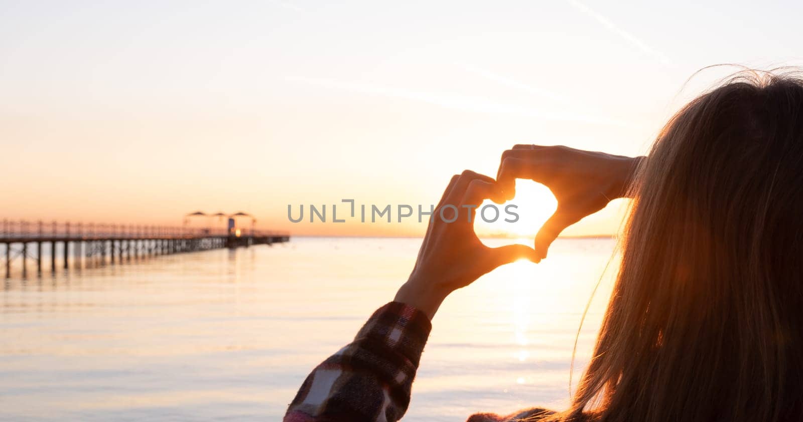 hands forming a heart shape with sunset silhouette on the beach