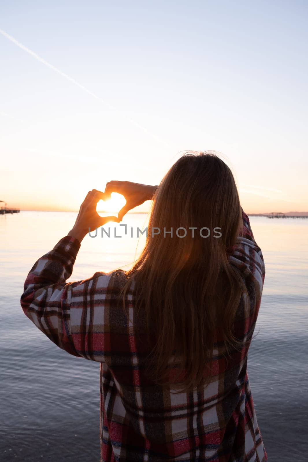 hands forming a heart shape with sunset silhouette on the beach