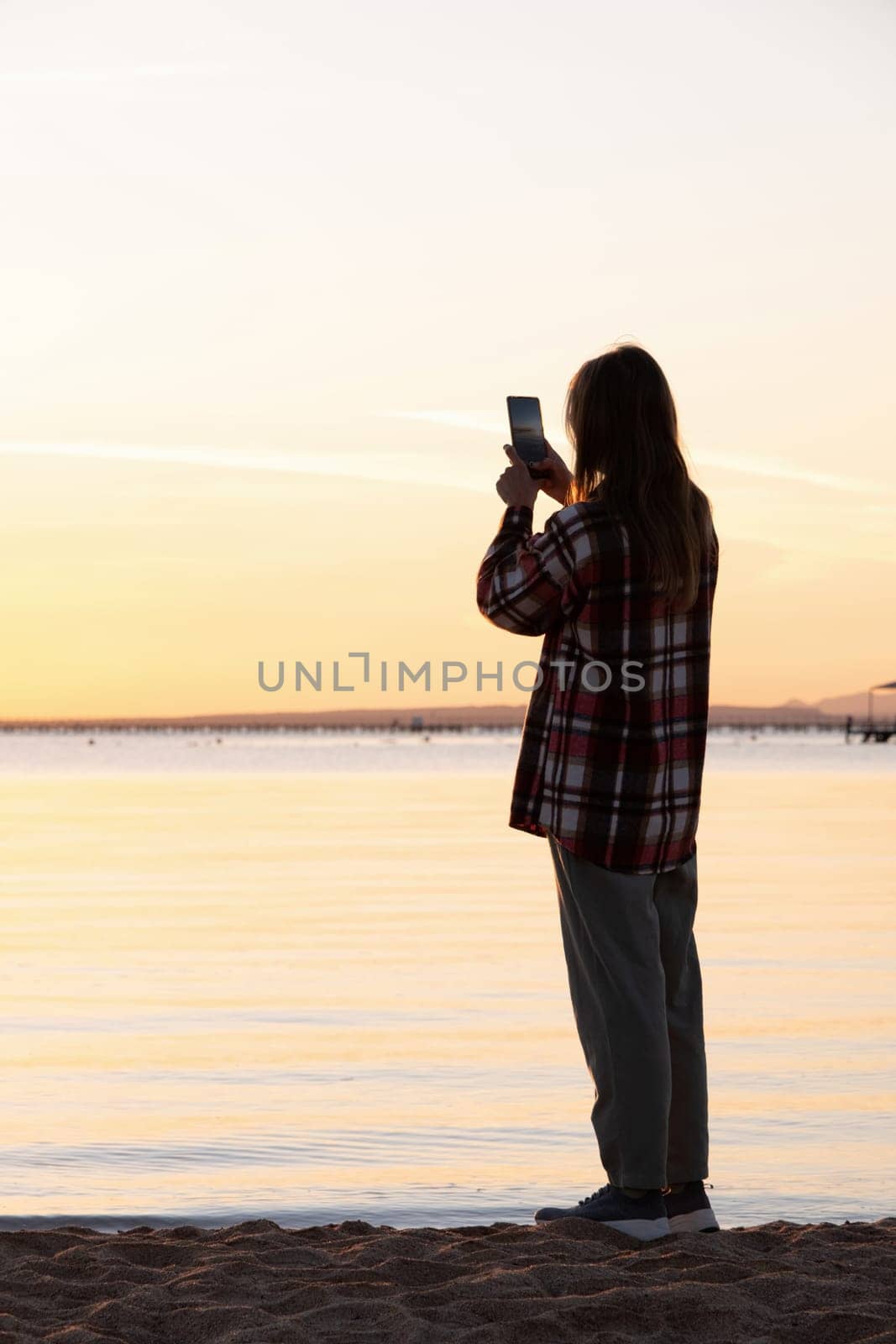 silhouette of woman taking a picture of sunrise on the beach by Desperada