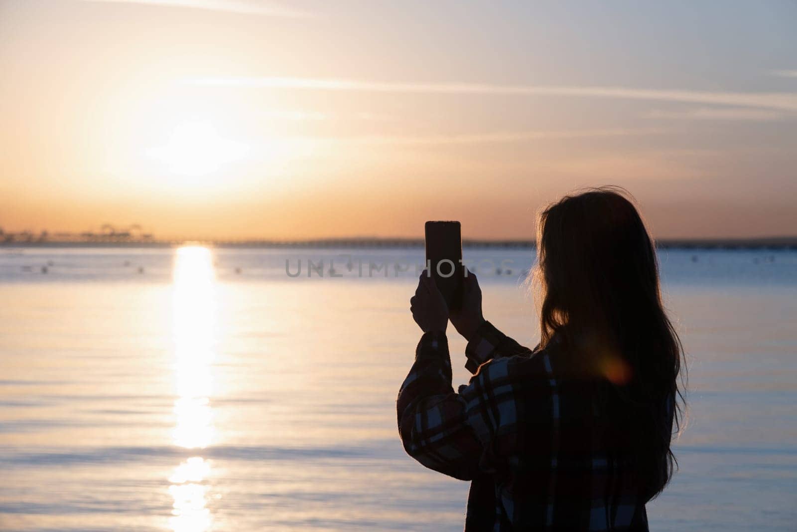 silhouette of woman taking a mobile picture of sunrise on the beach