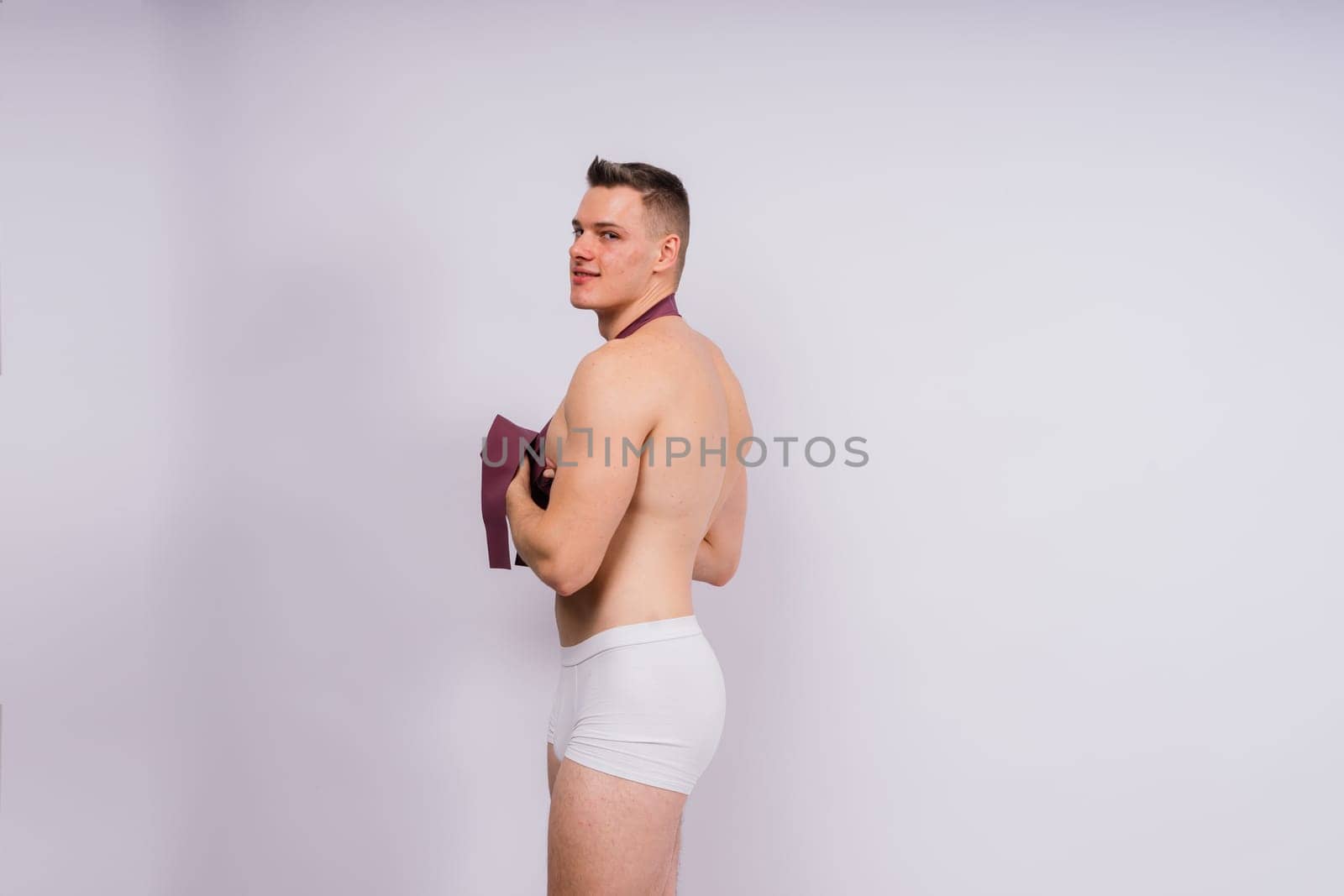 Young bodybuilder working out with rubber band over white and dark background by Zelenin