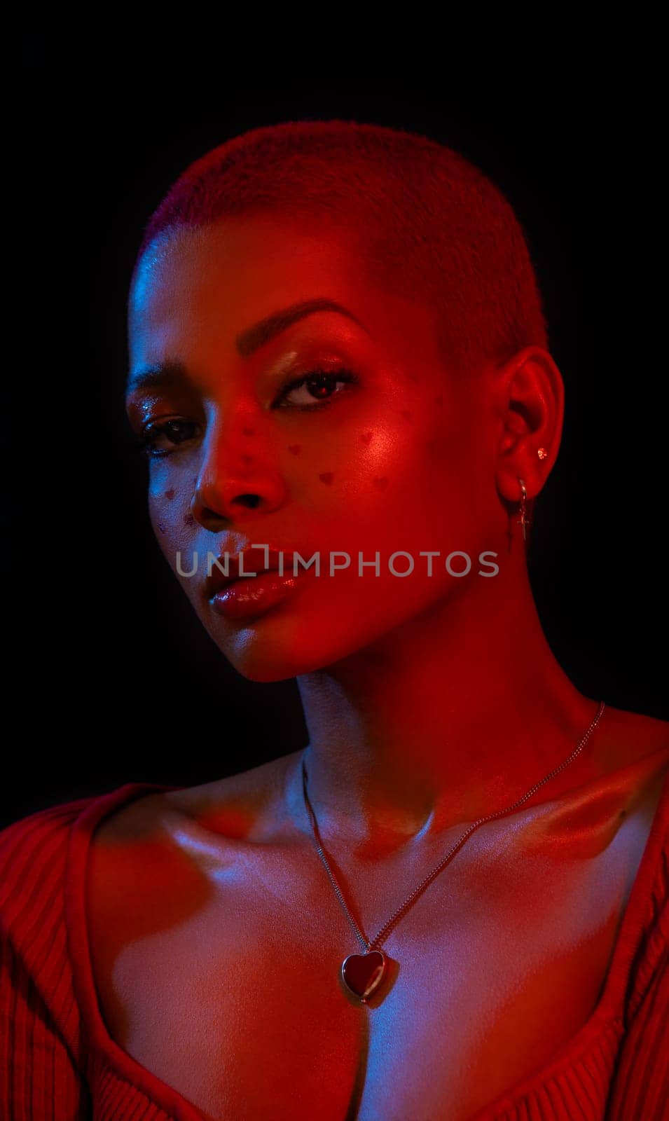 Creative makeup for Valentines day. Portrait of female fashion model in red neon light on black studio background. Beautiful woman with spring makeup in the shape of small hearts. Beauty concept
