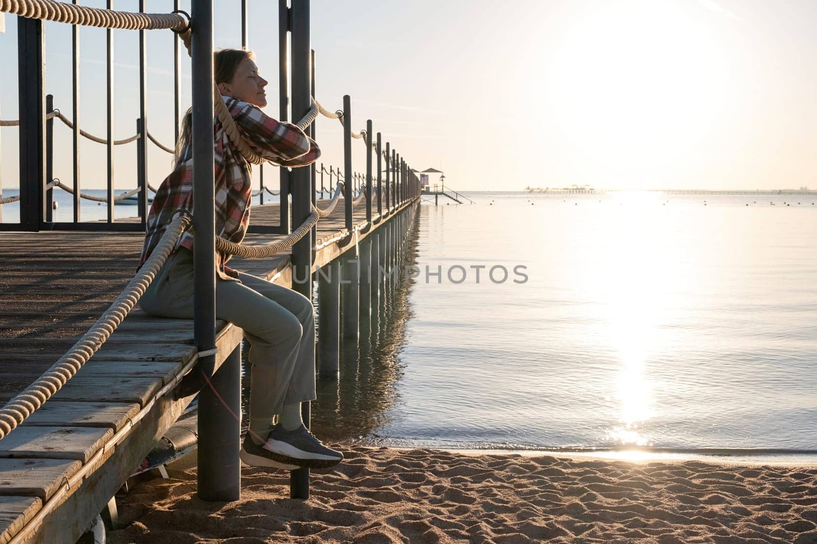 Young Woman sitting on a pier in sunrise, enjoying the view by Desperada