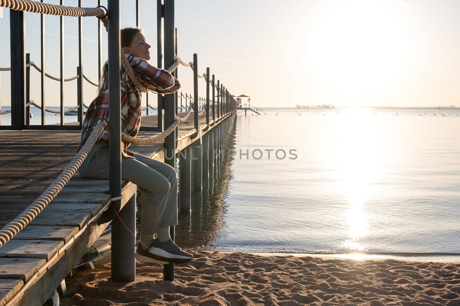 Travel and vacation. Young Woman sitting on a pier in sunrise, enjoying the view