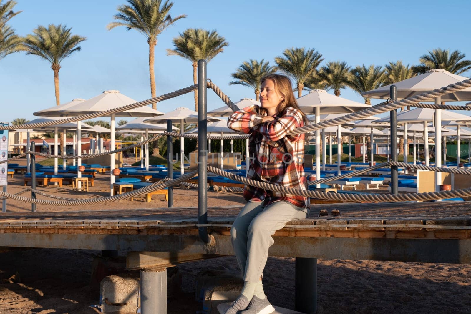 Young Woman sitting on a pier in sunrise, enjoying the view by Desperada