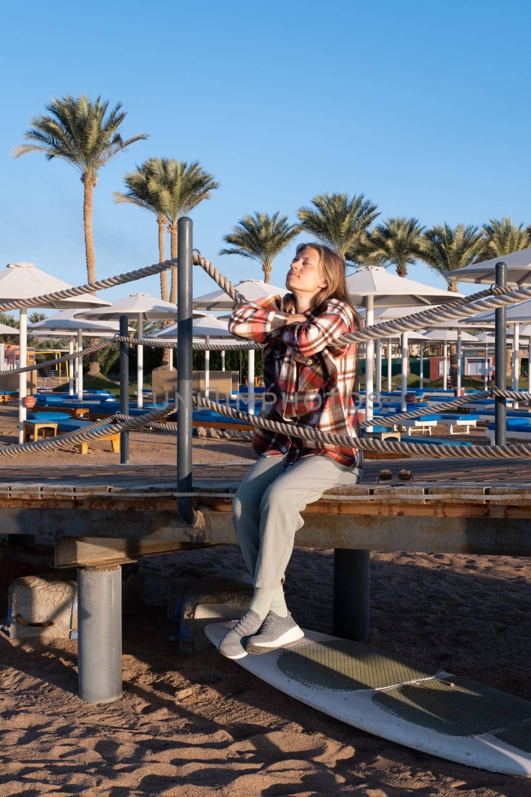 Young Woman sitting on a pier in sunrise, enjoying the view by Desperada