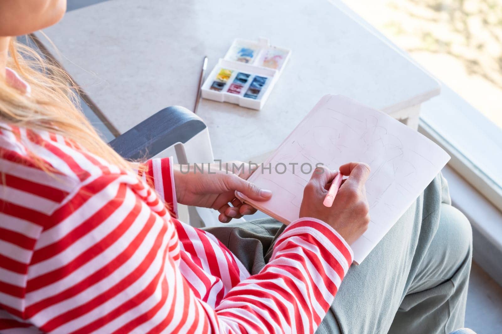 back view of a woman sketching in sketchbook sitting on the balcony by Desperada