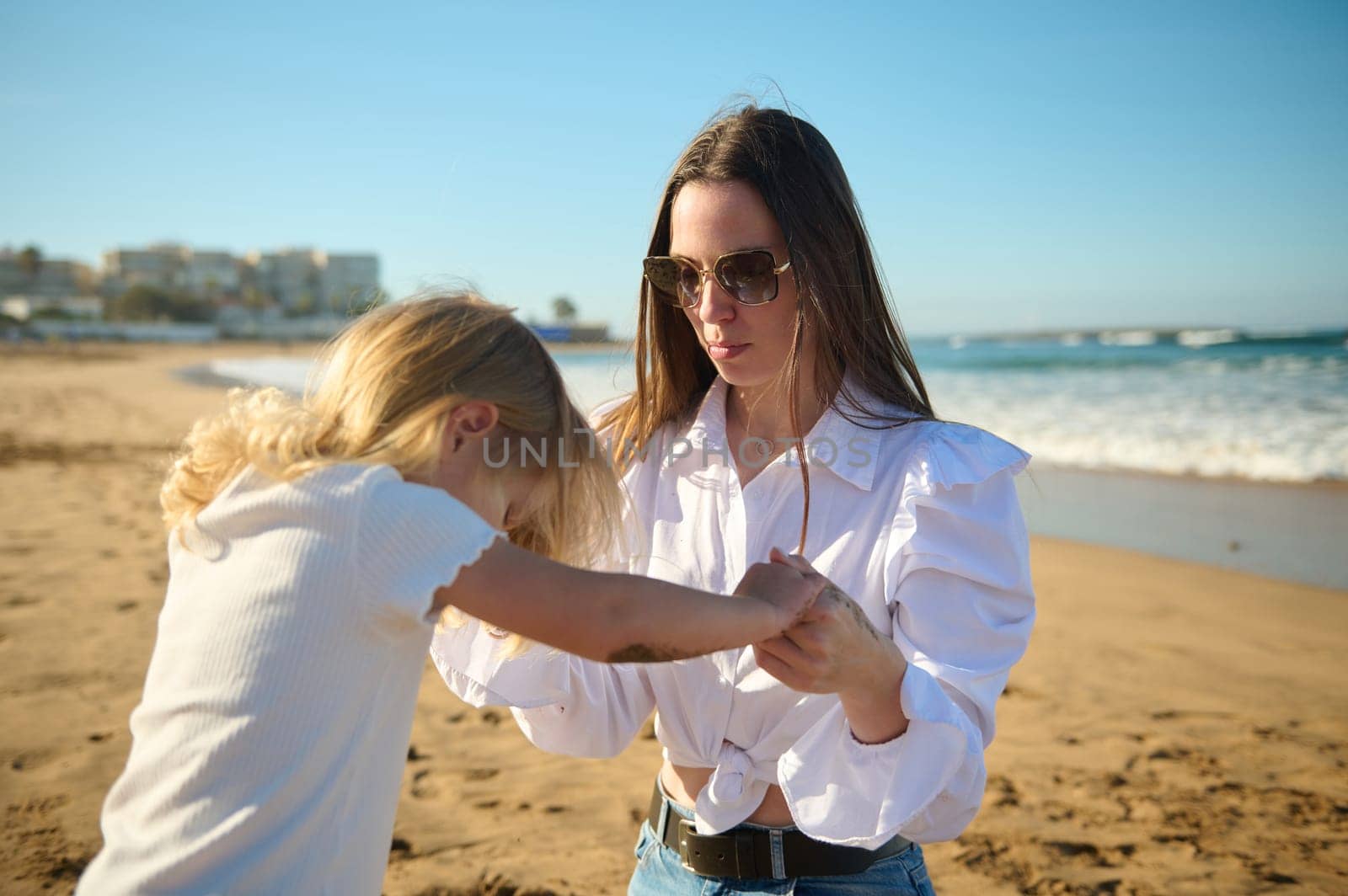 Mom and daughter holding hands while playing together on the beach on warm sunny day by artgf