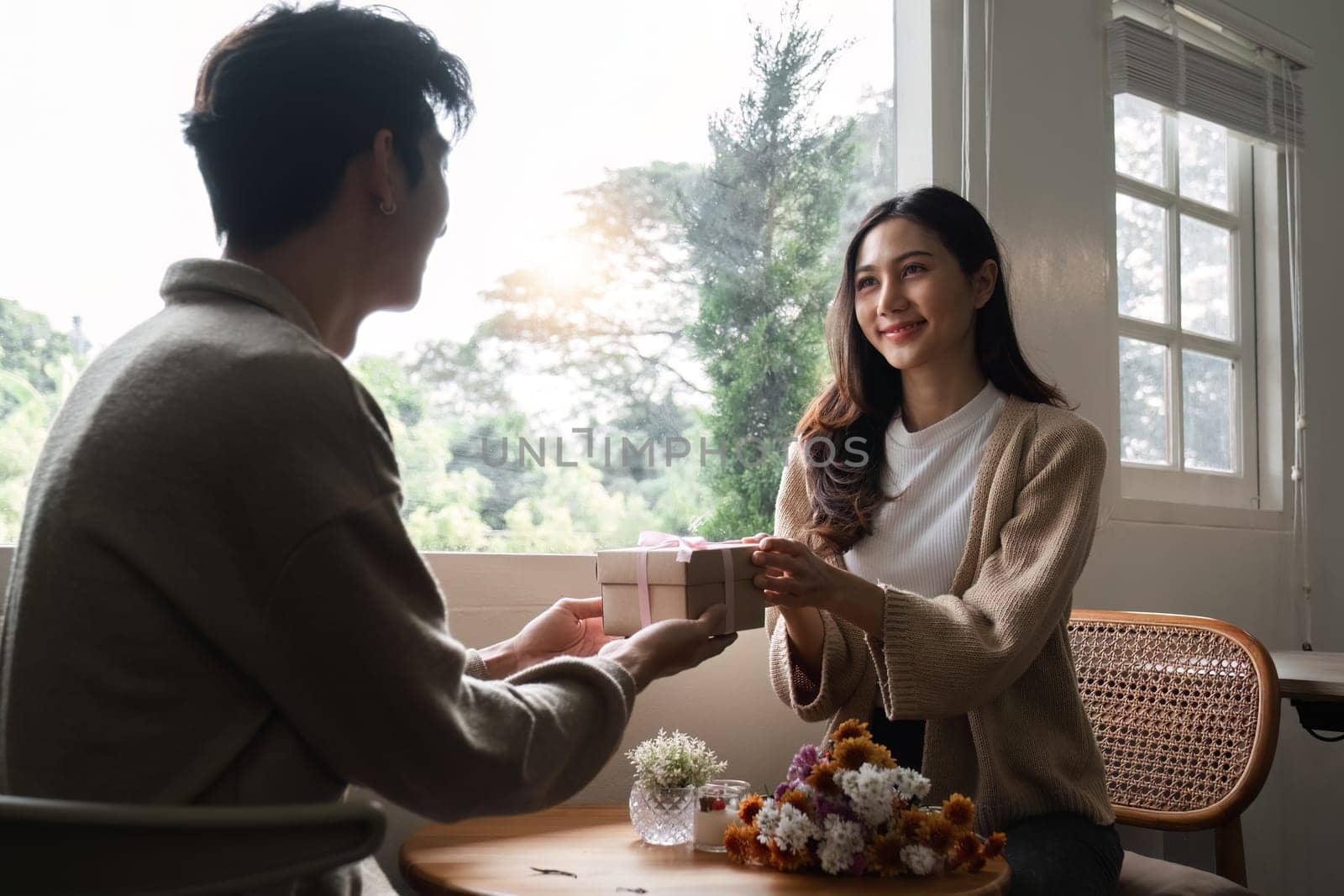 A young Asian couple gives each other gifts on their anniversary and sits happily together in the living room..