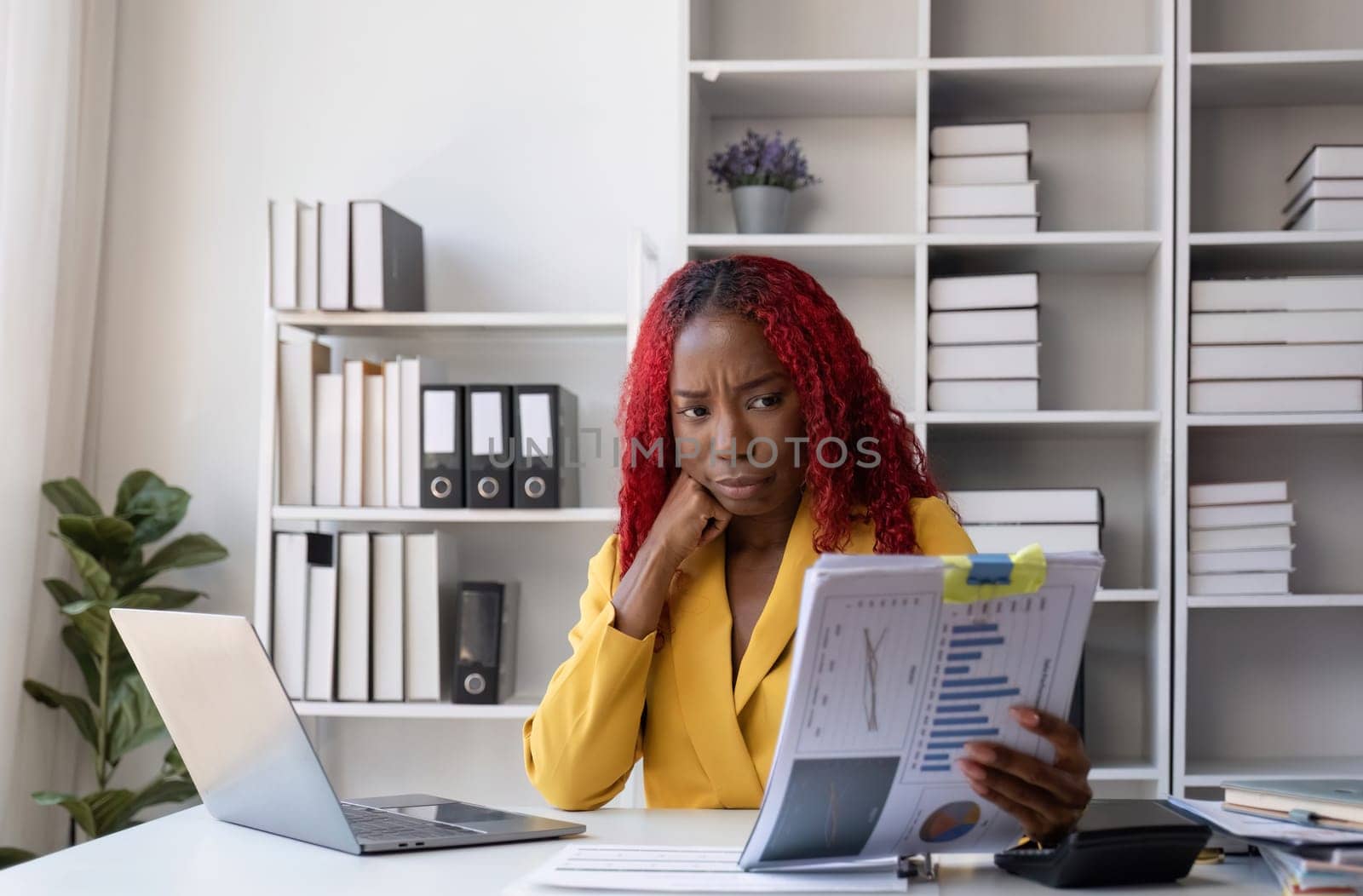 Young African American business woman uses a calculator to calculate numbers. Company financial accounts on desk in office by wichayada