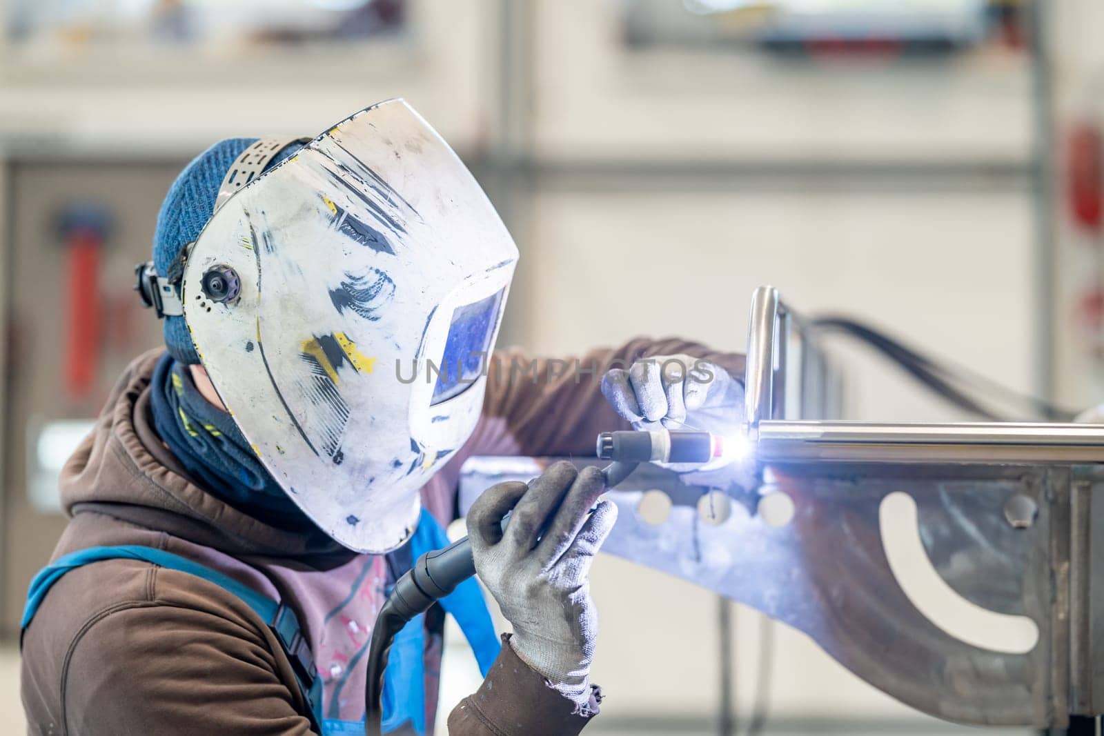 A man in personal protective equipment is welding metal in a factory by Edophoto