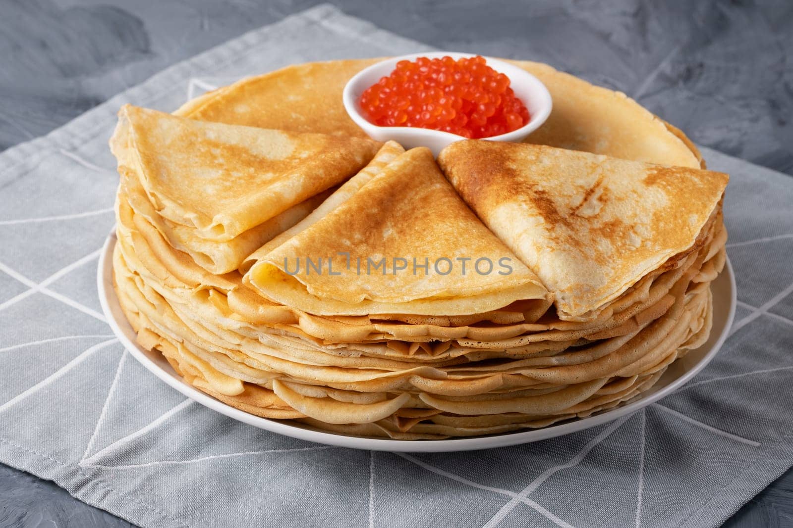 Pancakes with red caviar on grey background.