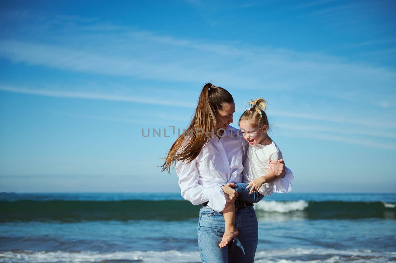 Happy loving mother carrying her child while walking together on the beach on a warm sunny day/ People. Family relationships. Motherhood and childhood concept