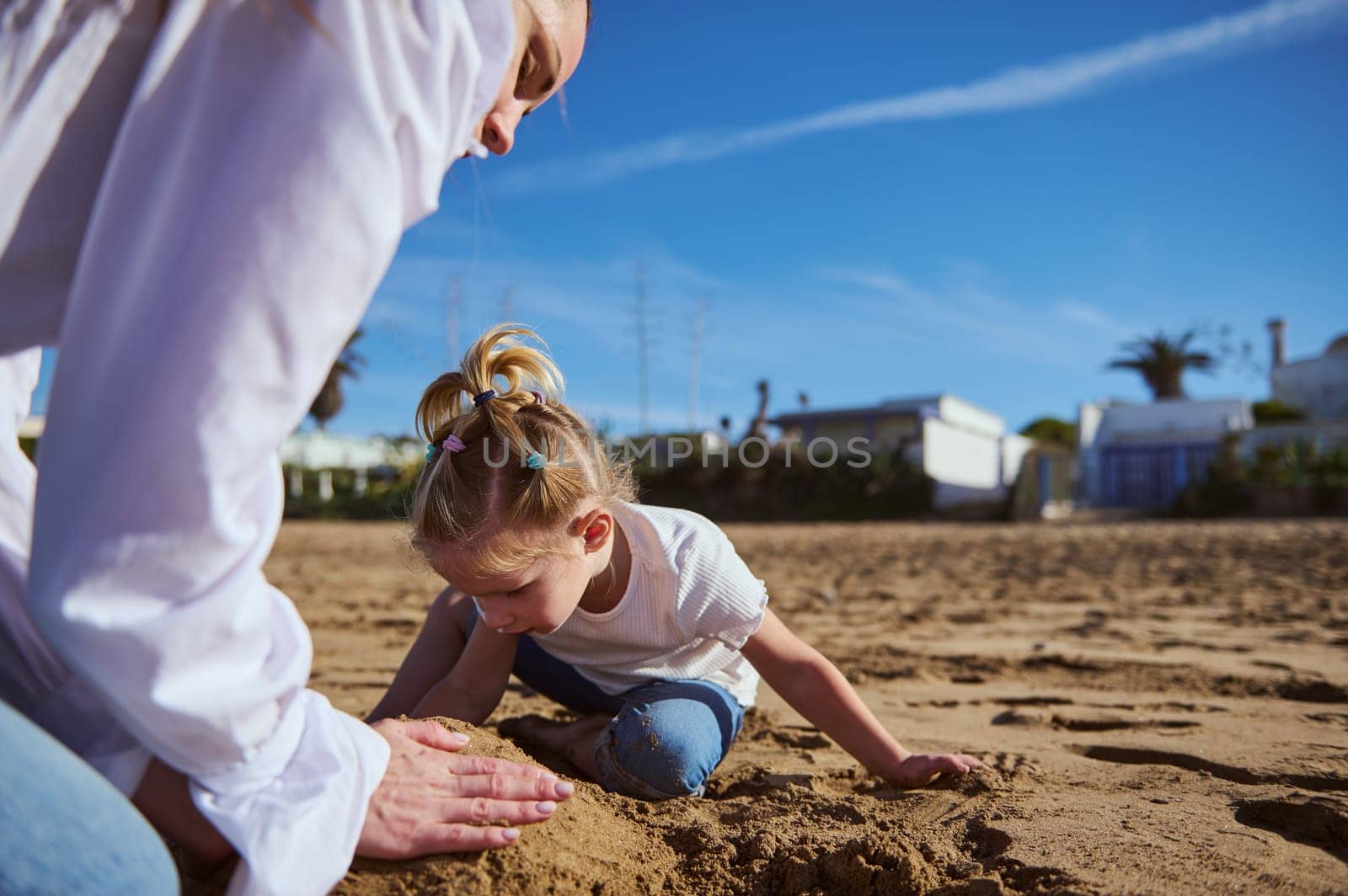 Mother and daughter playing on the beach together, building sand figures on the beach on warm sunny day. Happy family relationships concept
