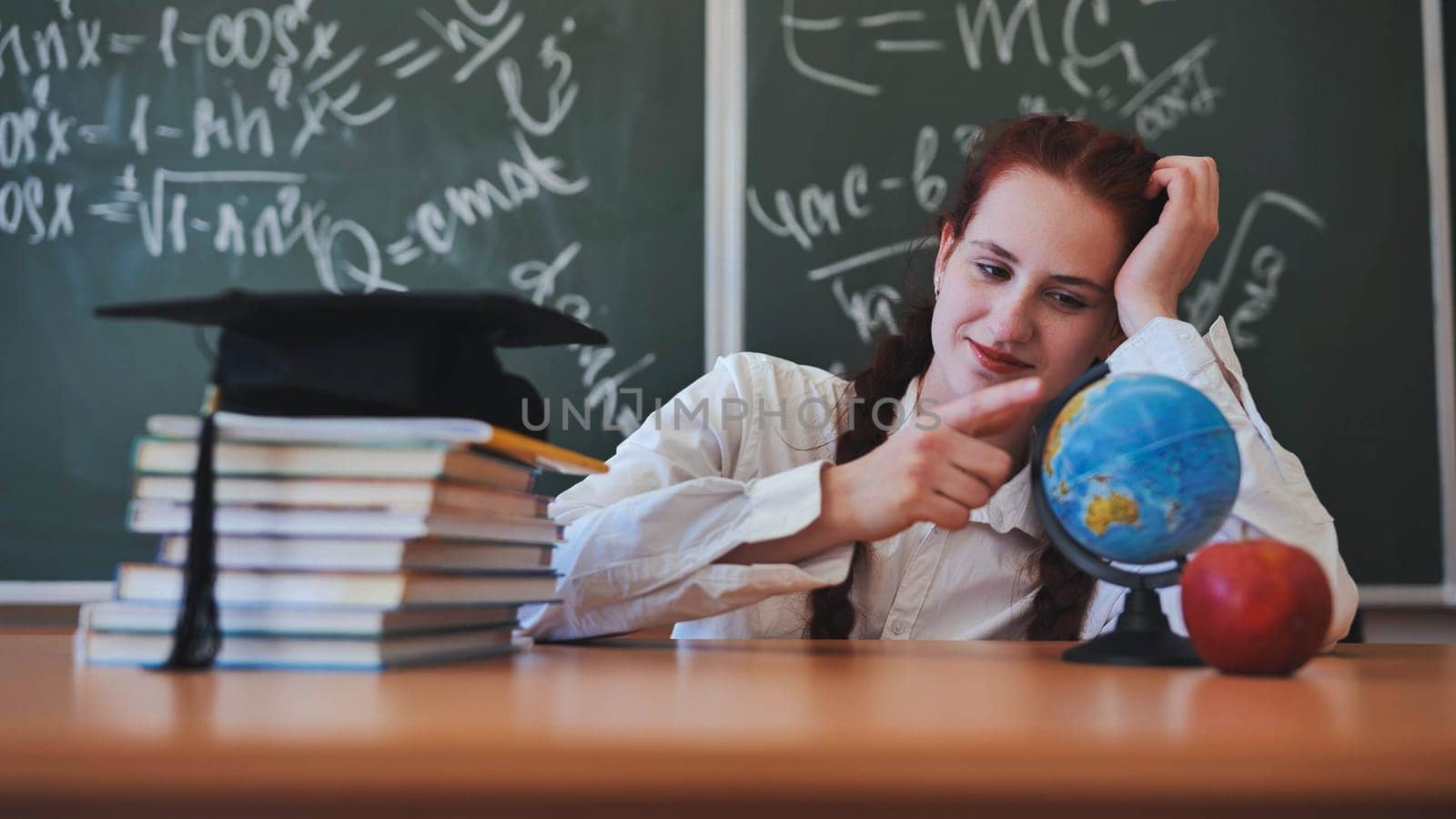 A redheaded schoolgirl poses and touches a globe