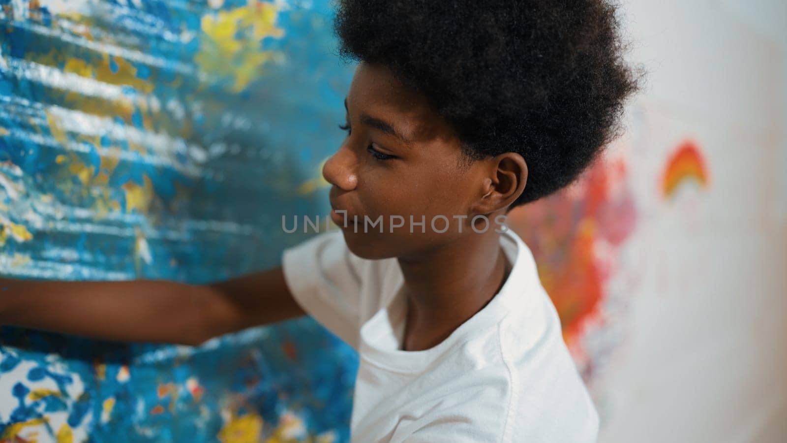 Side view of happy african boy painted the stained wall with colorful hand while wearing casual white shirt in art lesson.Smart student use hand print to make creative artwork. Education. Edification.