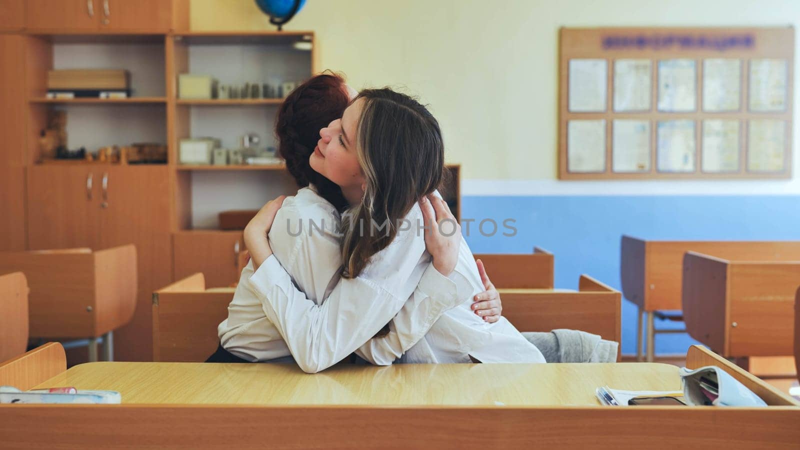 Girl students hugging in a classroom at school. by DovidPro