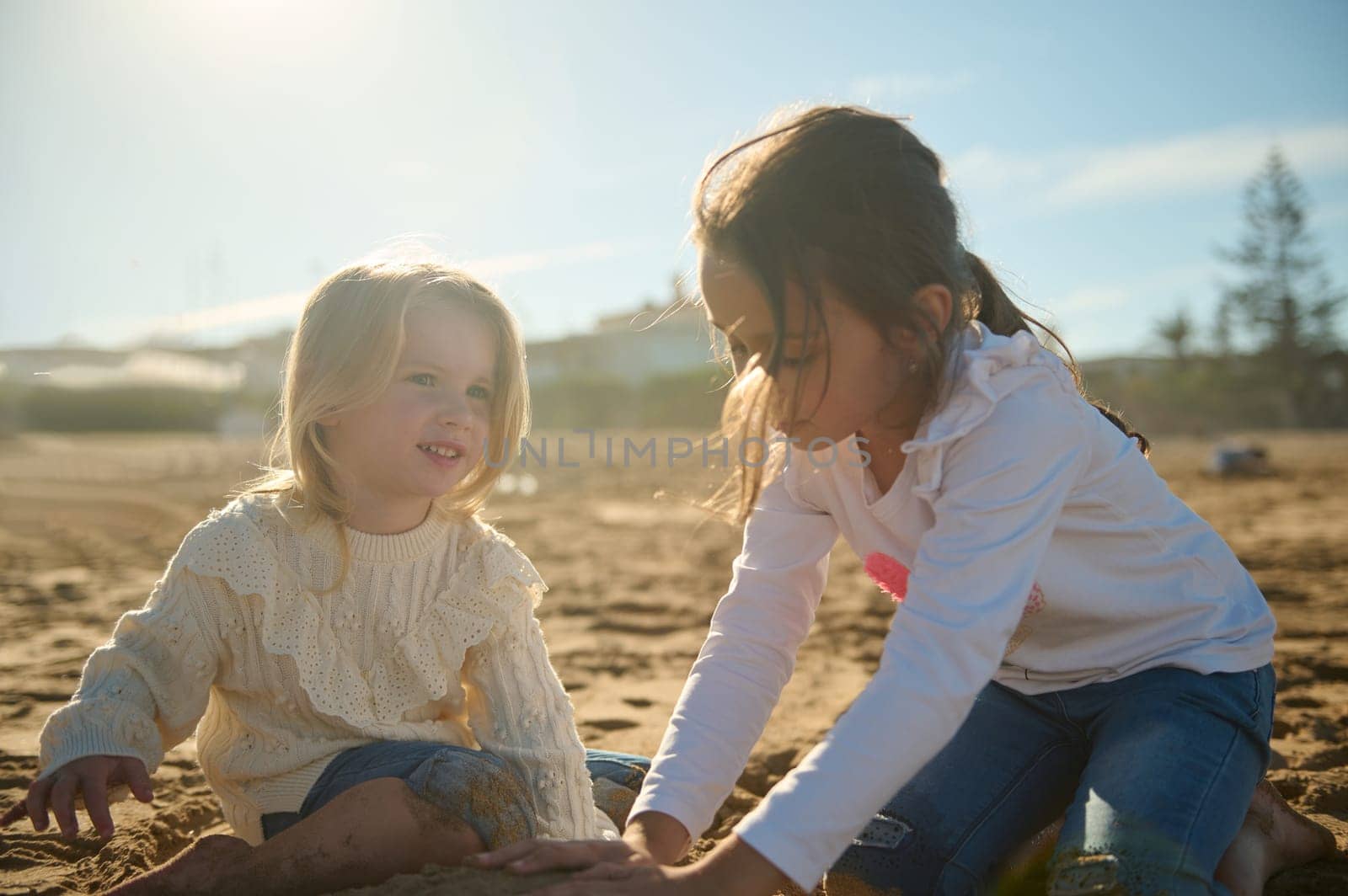 Caucasian adorable little kids girls playing together on the beach, building sandy castle on warm sunny day