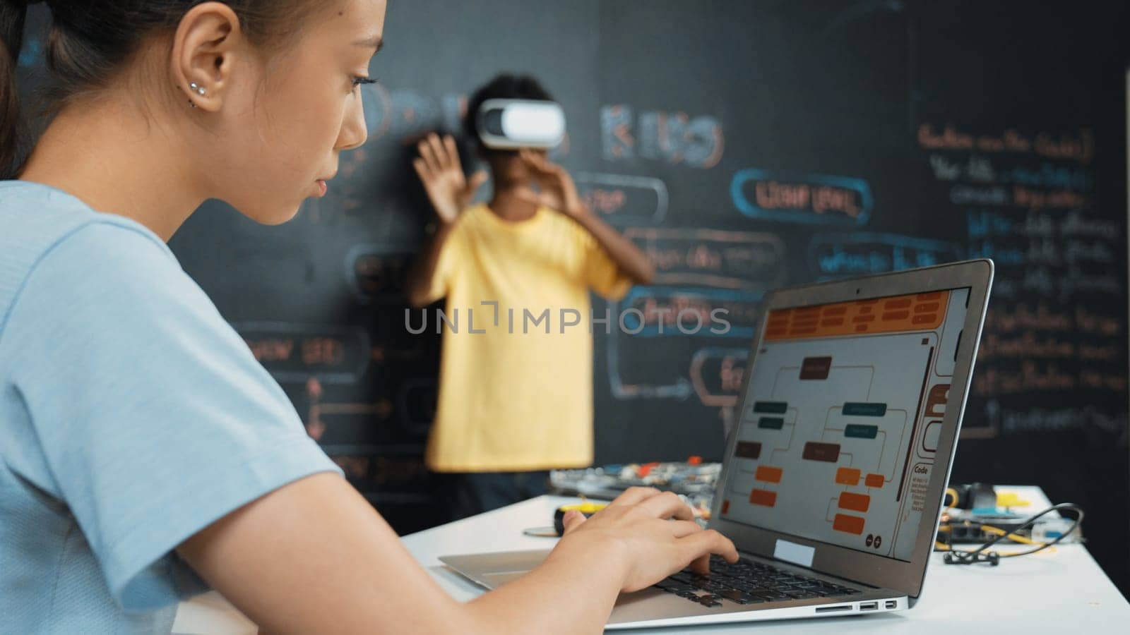 Closeup of school girl hand coding program while african student using VR interact with metaworld. Smart boy wearing virtual reality glasses and playing video games at innovative class. Edification.