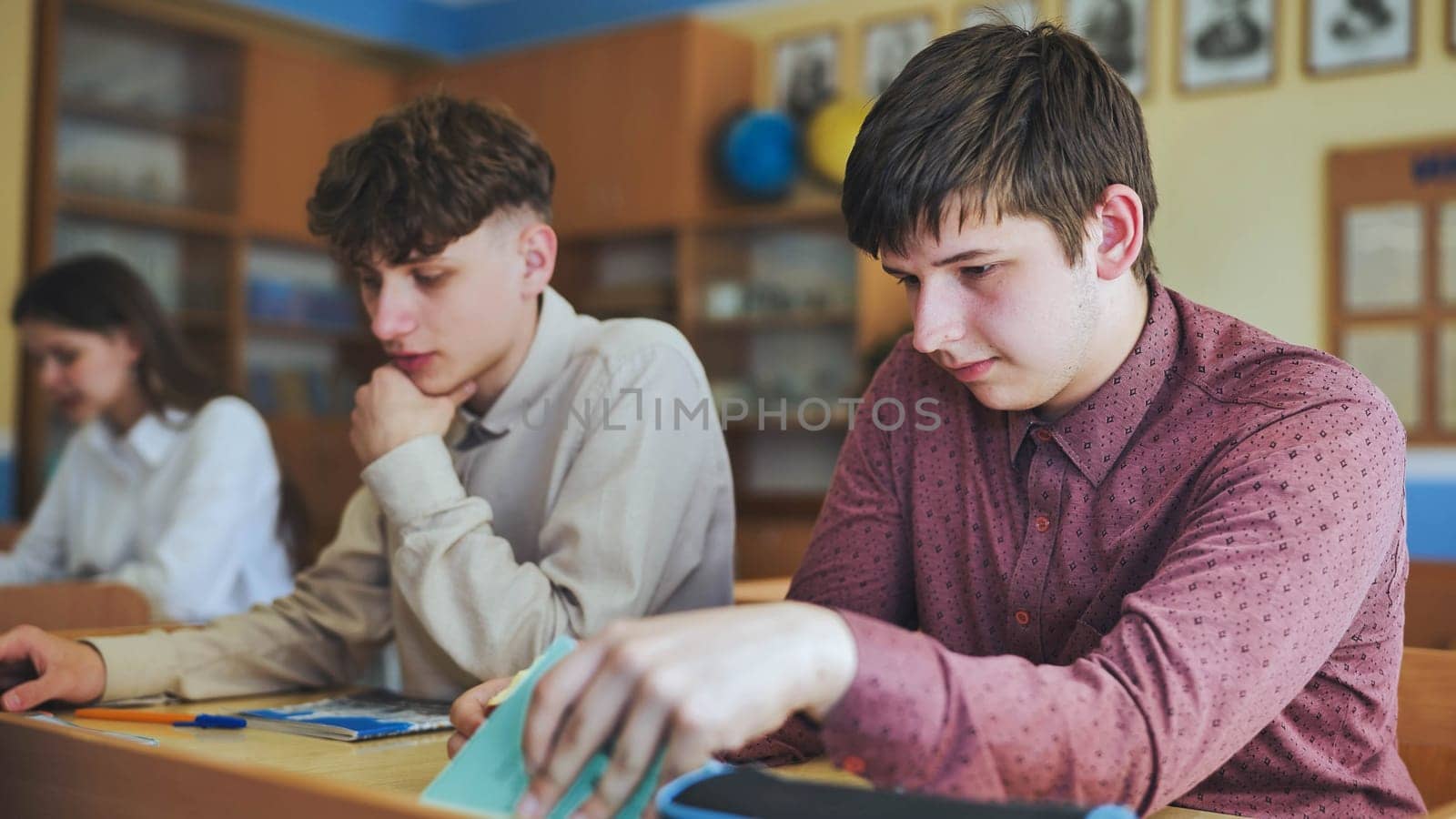 Schoolboys at a desk during class. The boy eats an apple. by DovidPro