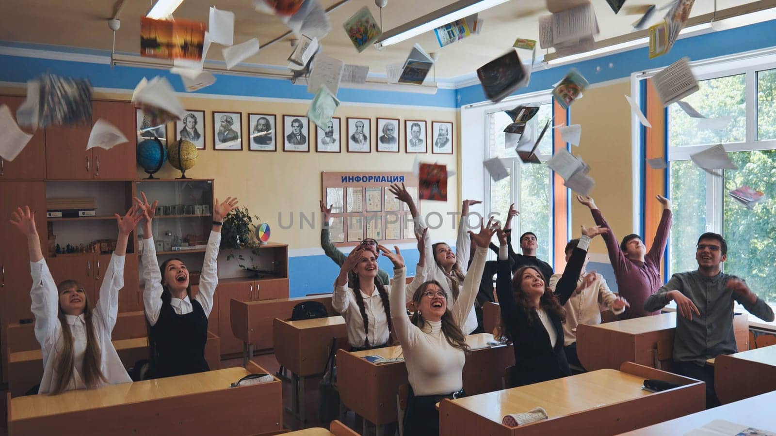 Berezovka, Belarus - May 15, 2023: Students toss notebooks and books up in their classroom. by DovidPro