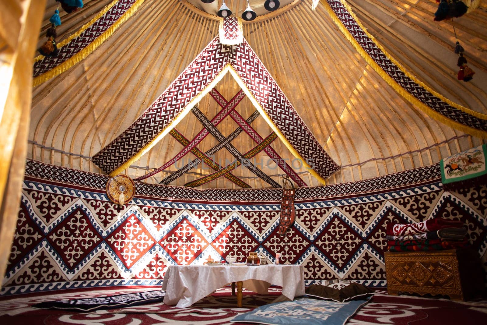 Interior of a Central Asian yurt with felt carpets, furniture, and a table. Traditional nomadic dwelling with white tablecloth.