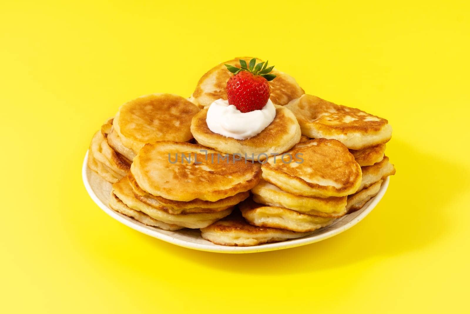 Mini pancakes with strawberries and sour cream on a yellow background.