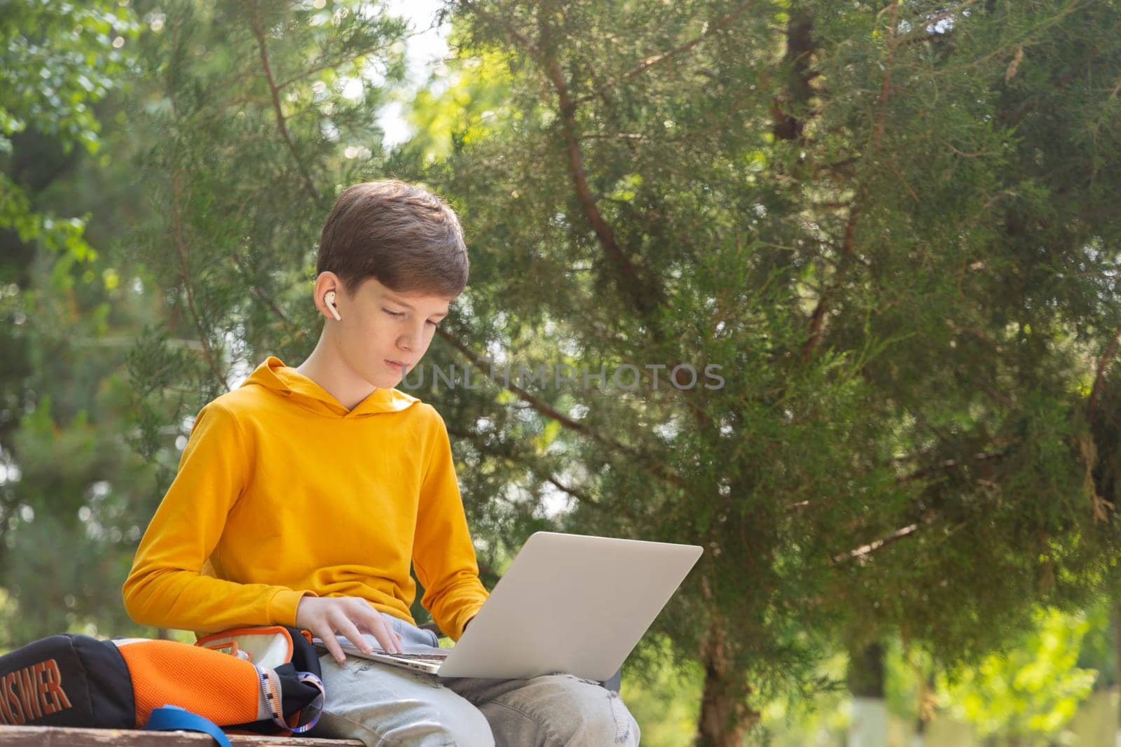 Thoughtful teenager boy resting. Holding and using a laptop for networking on a sunny day, outdoors. by Ri6ka