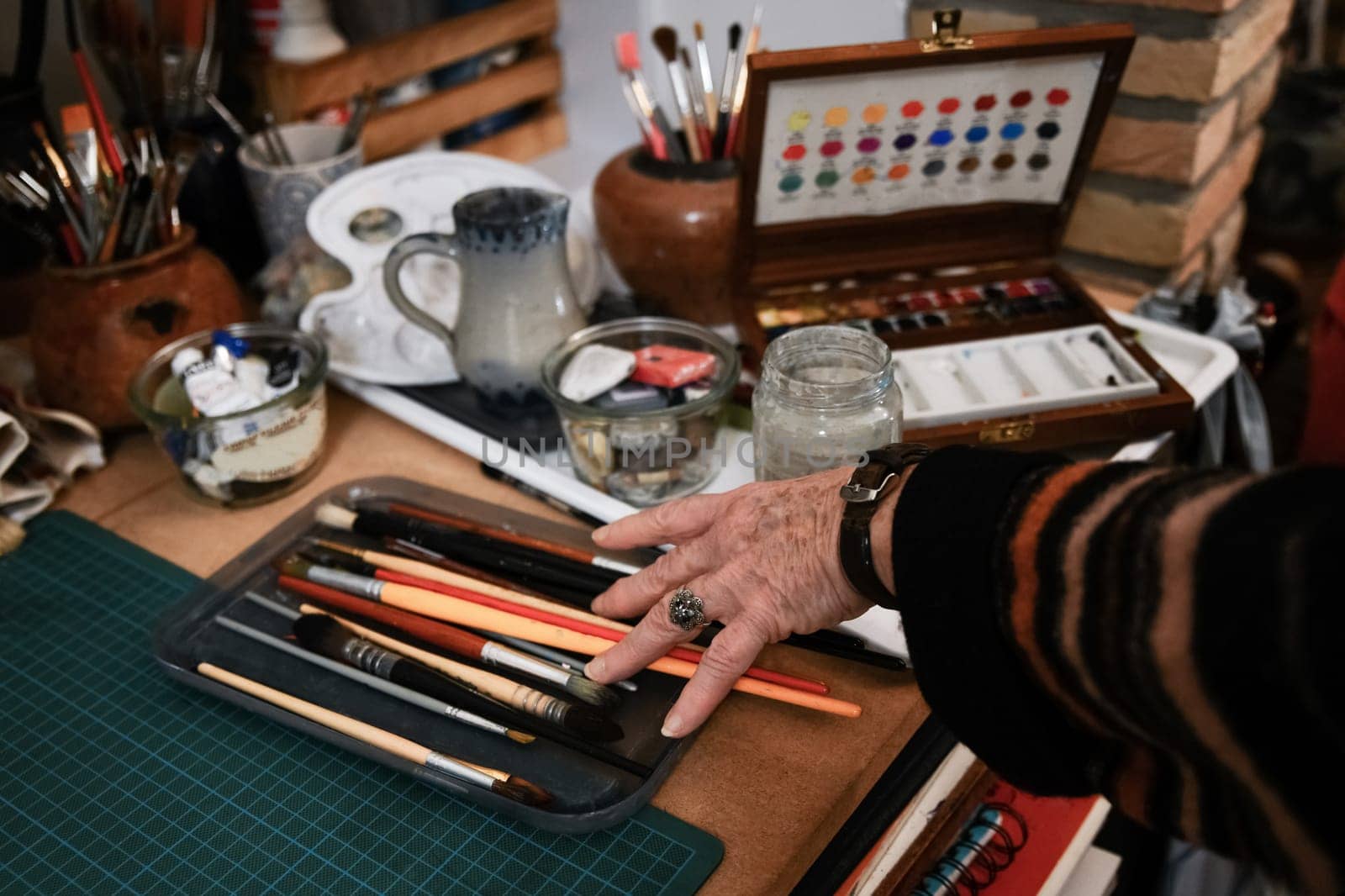 Old woman's hand takes paintbrushes for watercolor painting by Godi