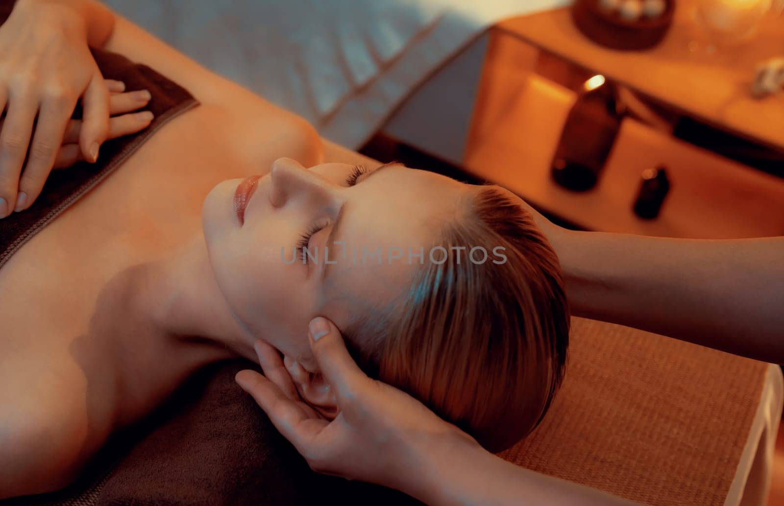 Caucasian woman enjoying relaxing anti-stress head massage and pampering facial beauty skin recreation leisure in warm candle lighting ambient salon spa in luxury resort or hotel. Quiescent