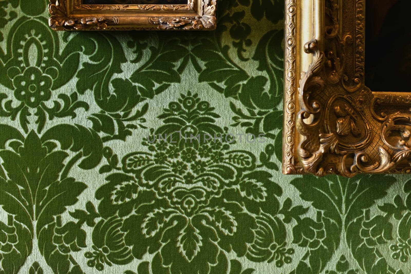 Green velvet wallpaper and gold frames with paintings in castle